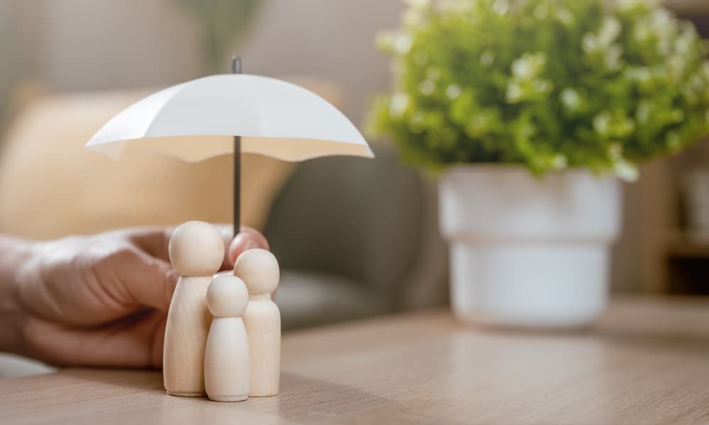 Assurance Famille: Sécurité et Protection de vos proches Parapluie blanc protégeant trois figurines en bois (famille) sur une table. Symbole d'assurance, de sécurité et de protection familiale.