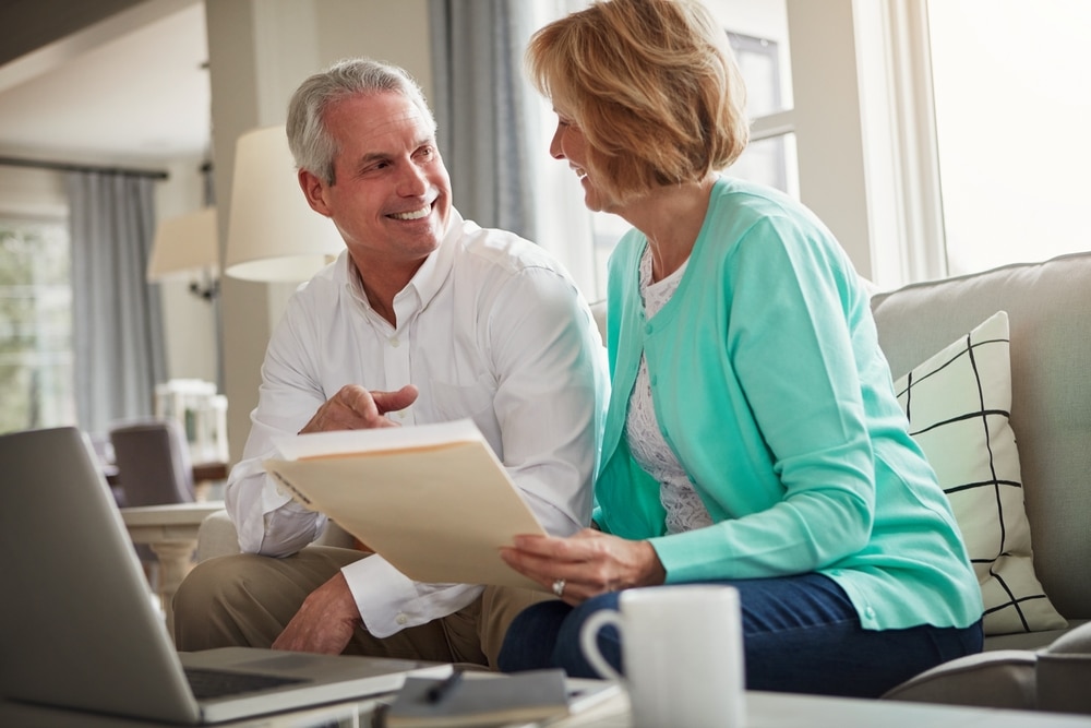 Un couple senior heureux planifie sa retraite dans le salon, consultant des documents et utilisant un ordinateur portable.